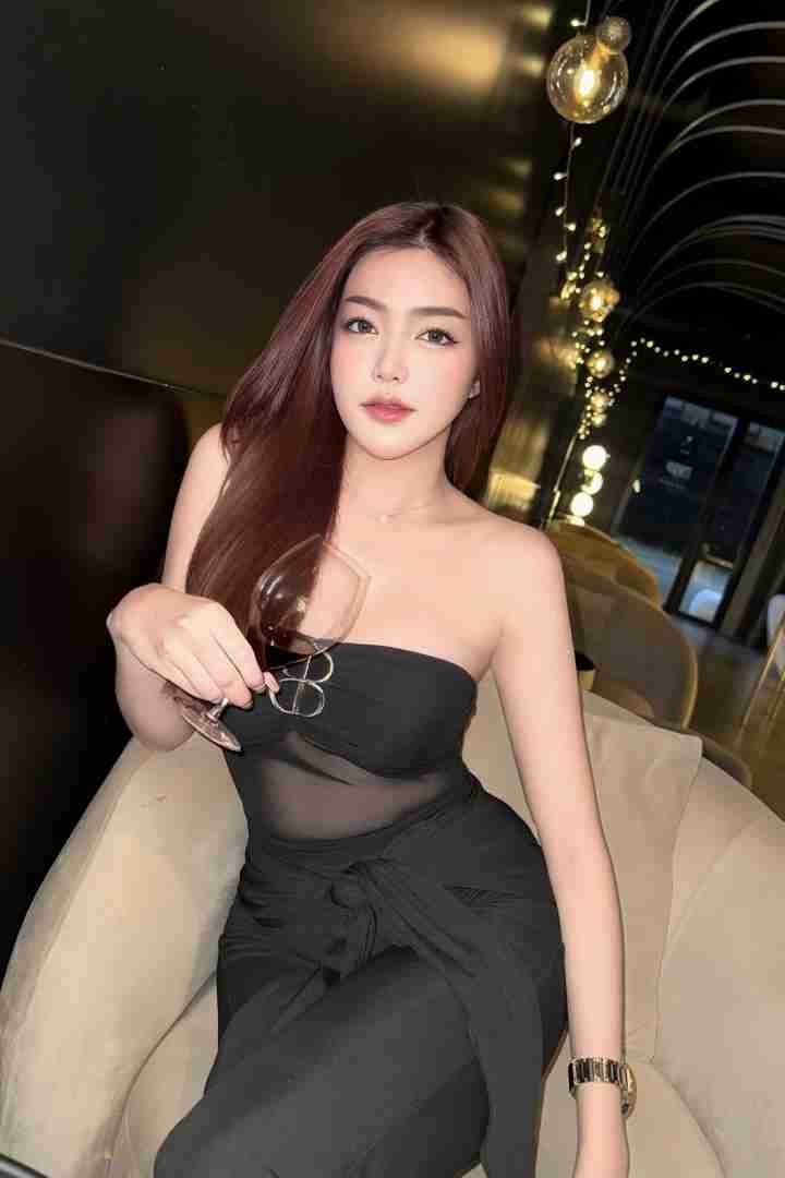 KL Escort Girl Woman in black dress holding glass of wine, seated indoors. Sex Call Girl