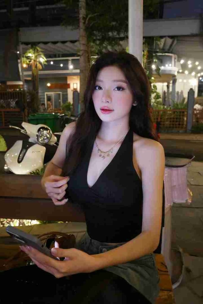 KL Escort Girl Woman in black halter top sitting outside at night, holding phone Sex Call Girl