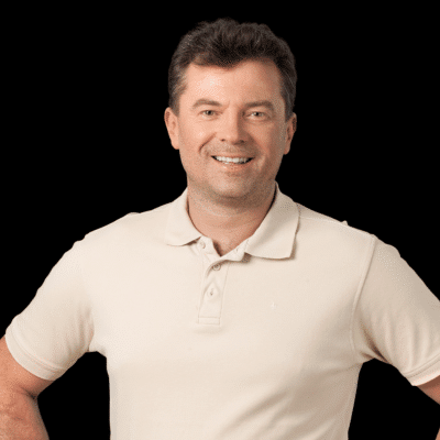 Smiling man in polo shirt with hands on hips, looking at camera against a black background.