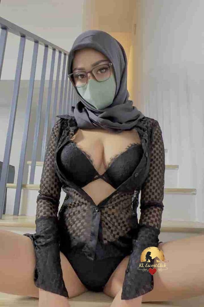 Aila in lingerie and hijab, sitting on stairs. Passionate Malay escort in KL.