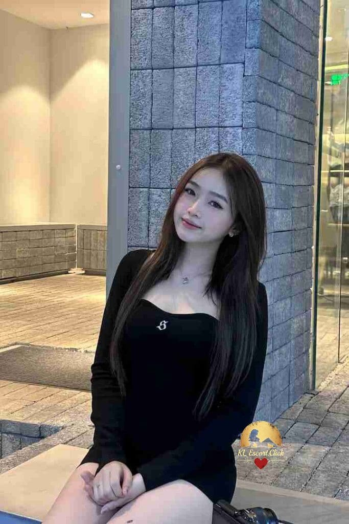 Attractive Asian woman in black dress smiling; escort service.