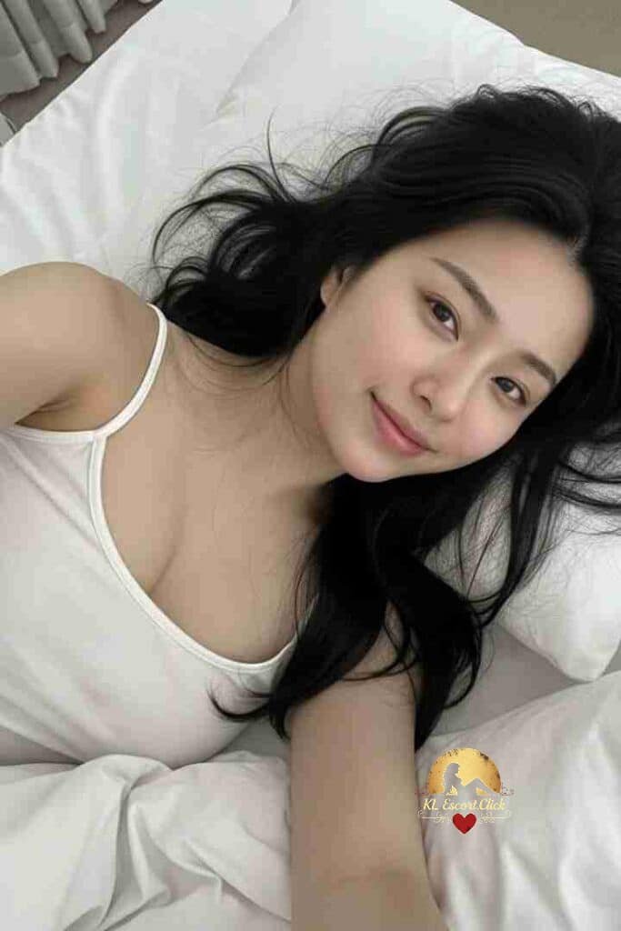 Beautiful Asian woman with black hair lying on white bed. Seductive KL Escort.