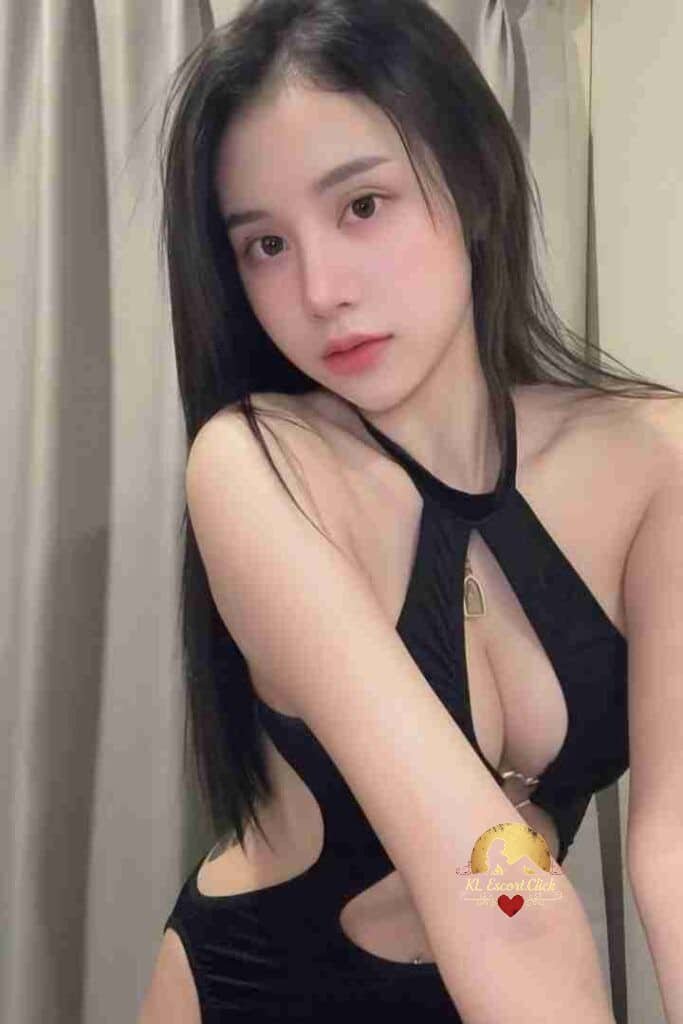 Attractive Asian woman in black halter swimsuit with cutouts posing indoors, looking at camera.