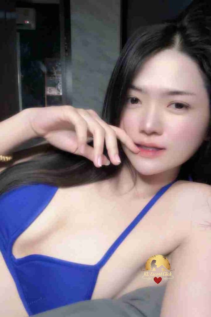 Attractive Asian woman in blue top posing with hand to face.