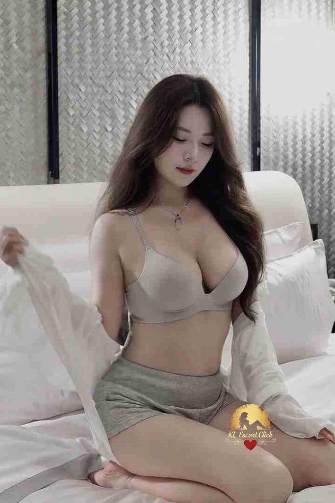 Relaxing Asian woman in bra and shorts sits on bed. Gentle, sensual pose.