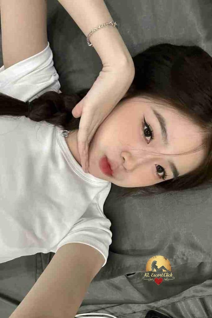 Pretty Asian woman with braid resting on grey sheets.