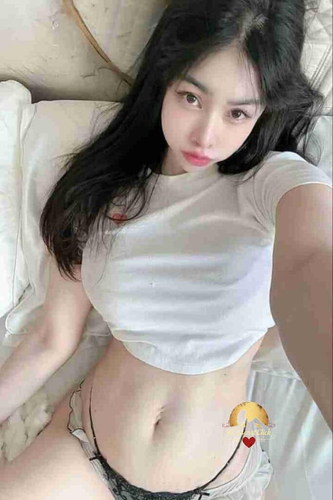 Asian woman in white crop top lying on bed, looking at the camera. Black hair, lingerie visible.