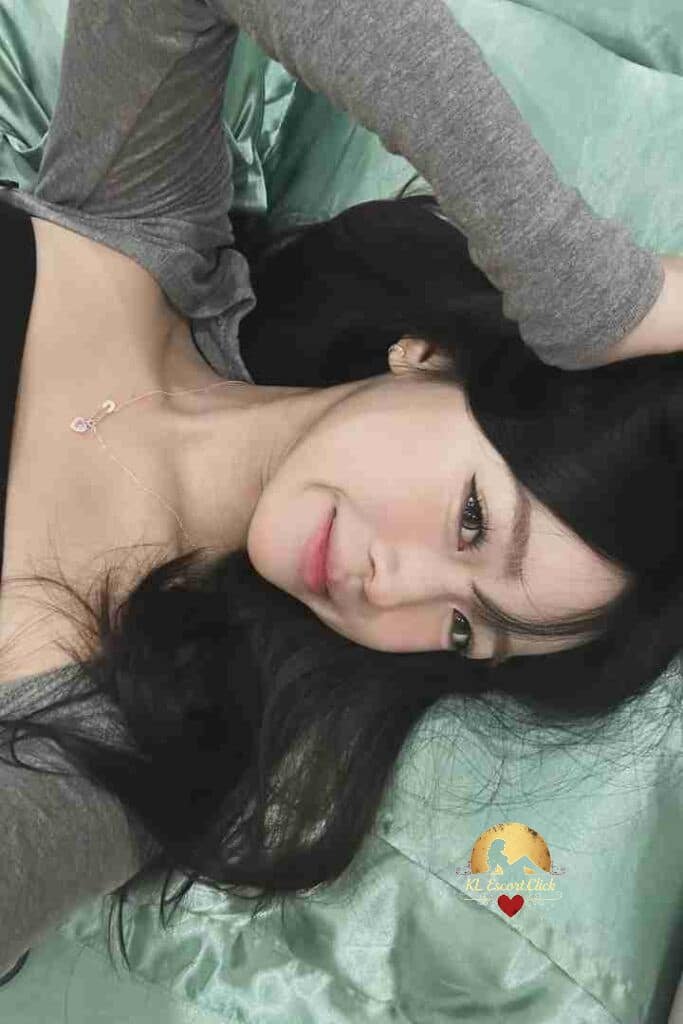 Attractive Asian woman with long black hair laying down, smiling subtly. Necklace visible.