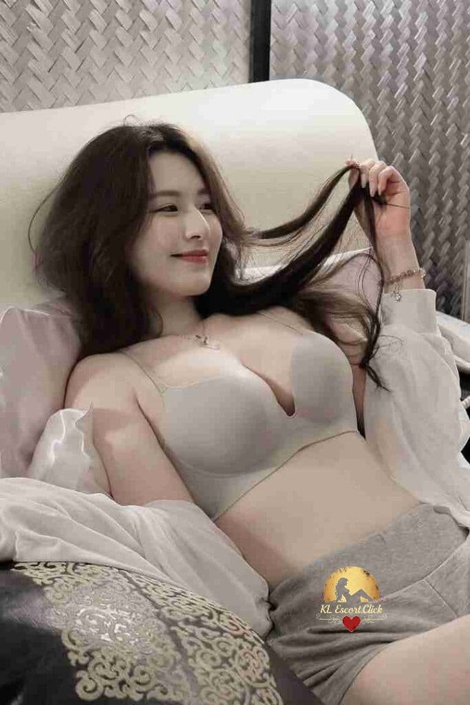 Relaxing Asian woman in bra and shorts lying on a couch, smiling gently.