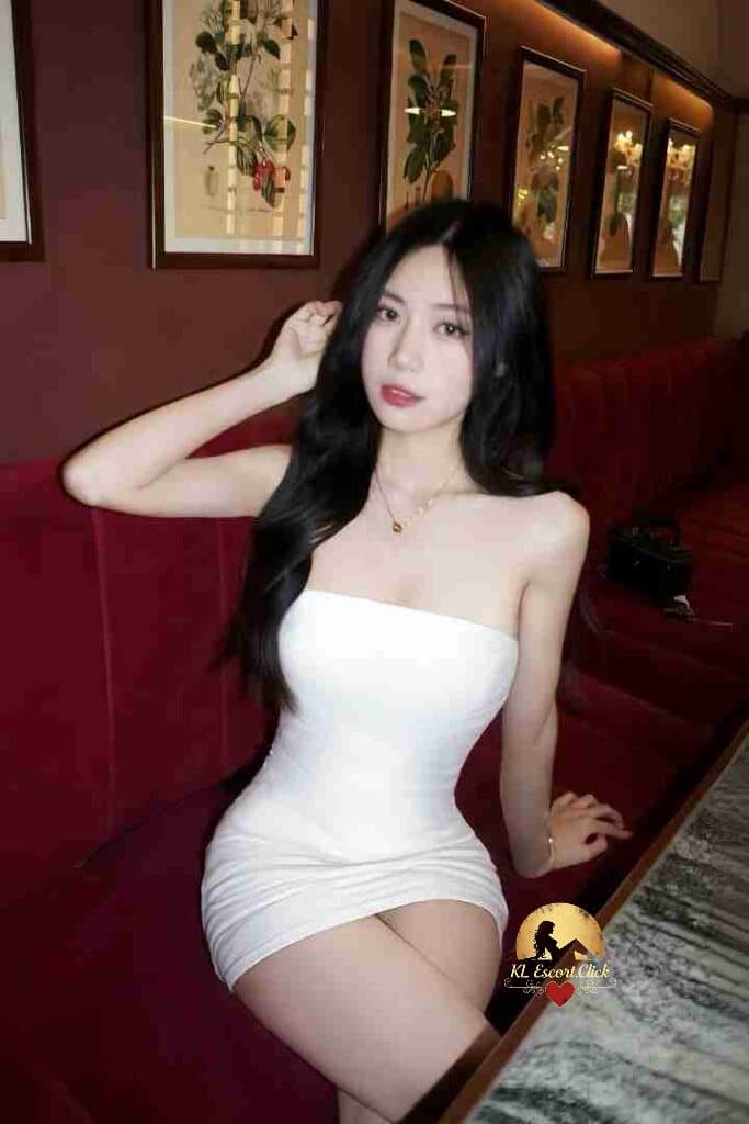 Attractive Asian woman in white dress sitting on red couch with artwork in background.