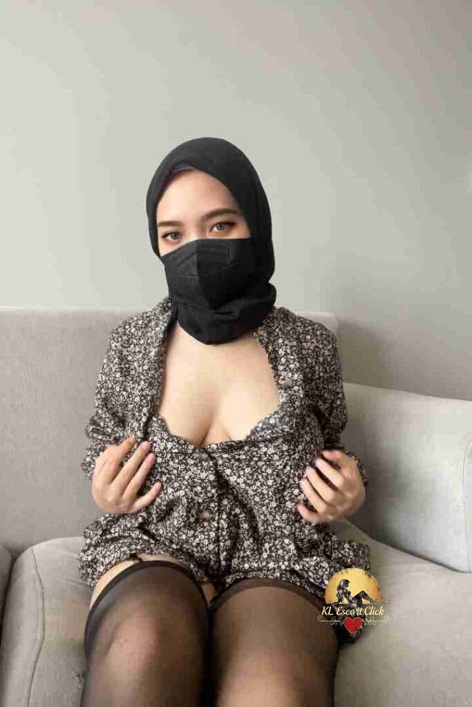 Malay woman in hijab and mask, floral dress, and stockings on couch.