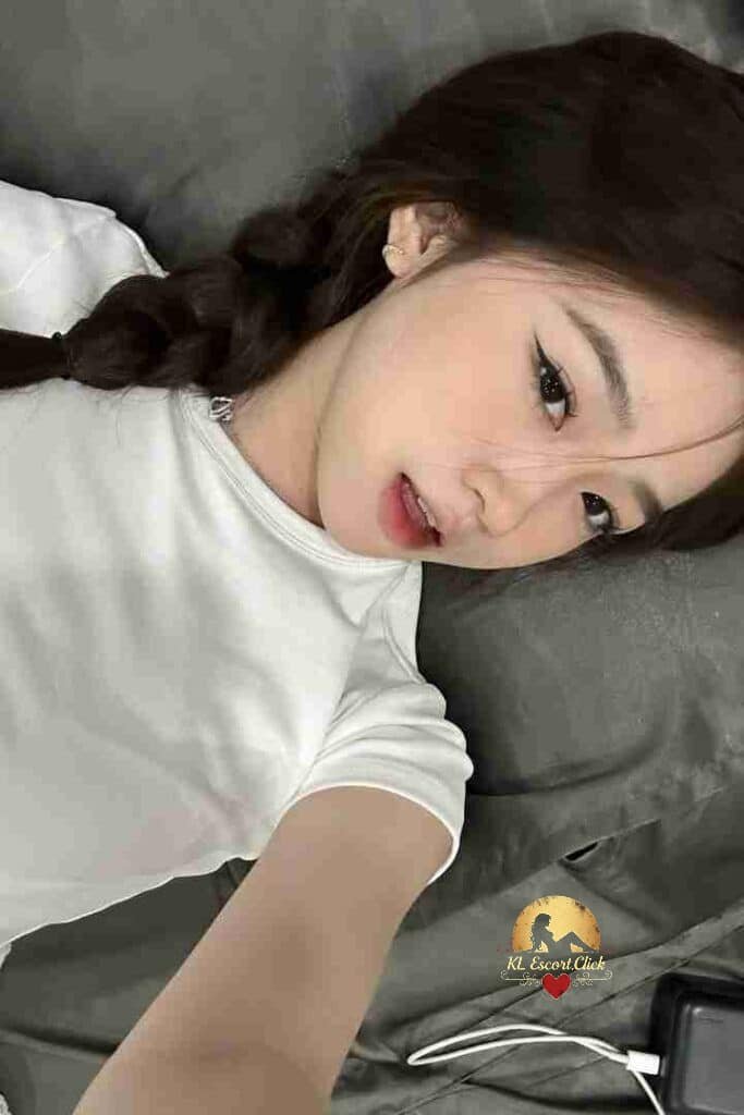 Pretty Vietnamese girl with braid, lying on a bed. C-cup, KL Escort.