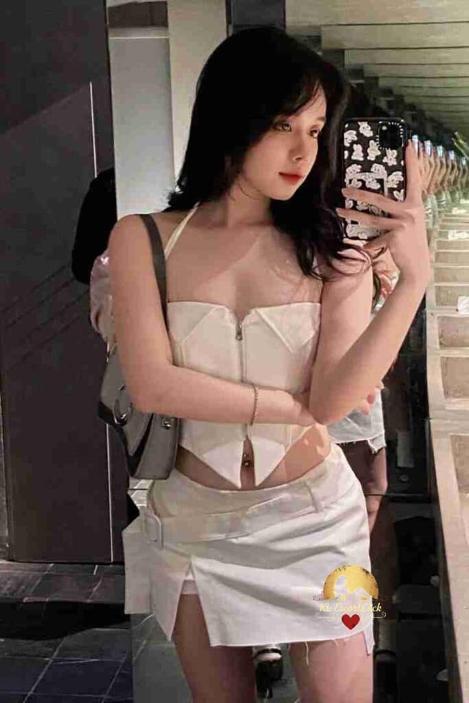 Vietnamese woman in white halter top and mini skirt takes mirror selfie. KL Escort Mia.