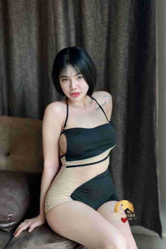 Woman in stylish black and beige swimsuit sitting indoors with short black hair and a tattoo on her arm.