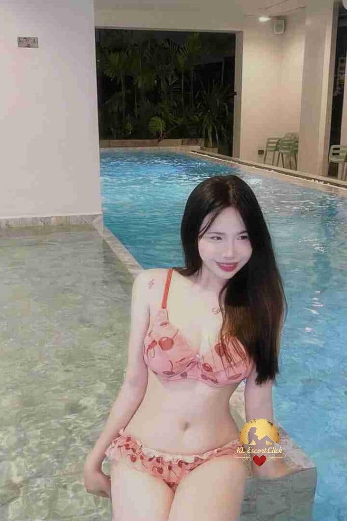 Woman in cherry print bikini by pool. Red lipstick, long dark hair, fair skin. Indoor swimming pool.