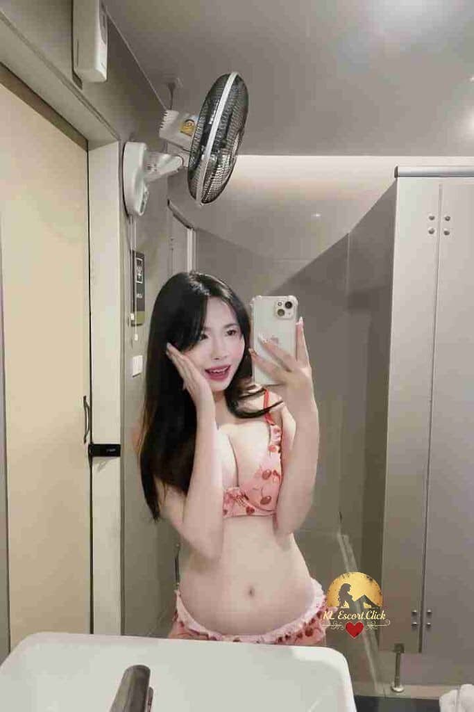 Woman in cherry print lingerie takes a selfie in a bathroom with a wall-mounted fan.
