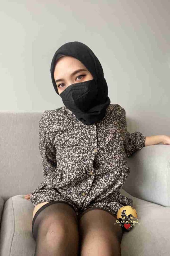 Woman in hijab, floral dress, and stockings sitting on couch.