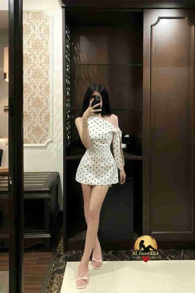 Woman in polka dot dress taking a mirror selfie in an elegant room with dark wood furniture.